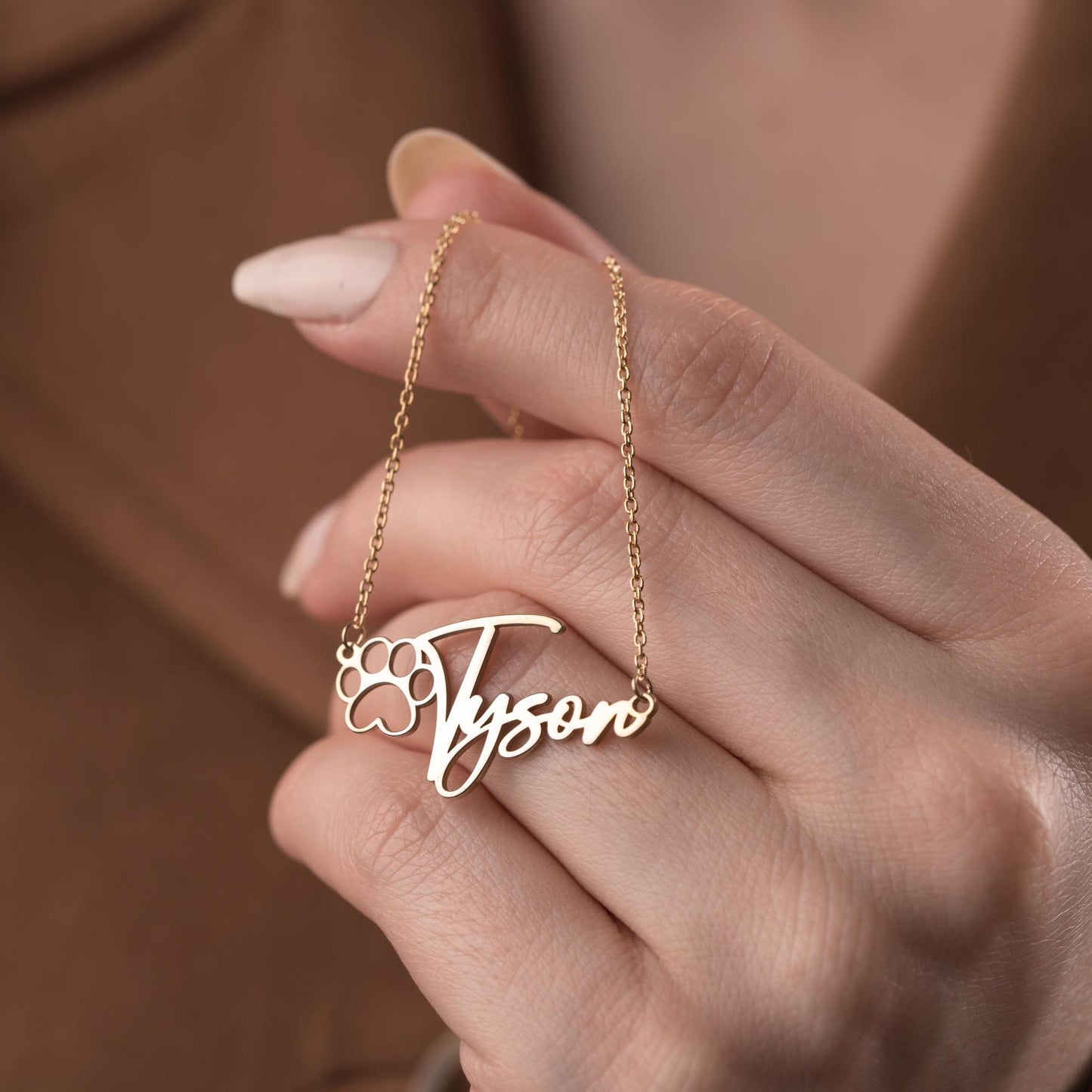 Custom pet name necklace with a paw print design in 925 sterling silver and 14k gold plated options, perfect for pet lovers. A personalized, handmade gift displayed on a soft fabric background.