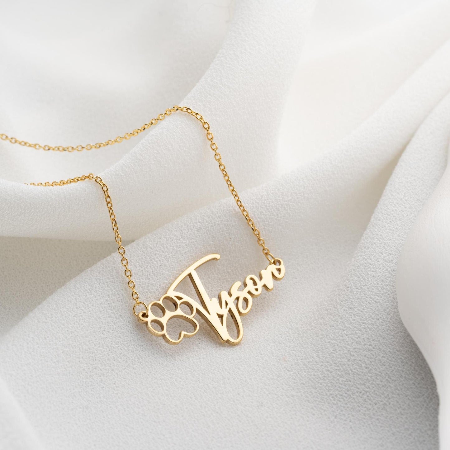 Custom pet name necklace with a paw print design in 925 sterling silver and 14k gold plated options, perfect for pet lovers. A personalized, handmade gift displayed on a soft fabric background.