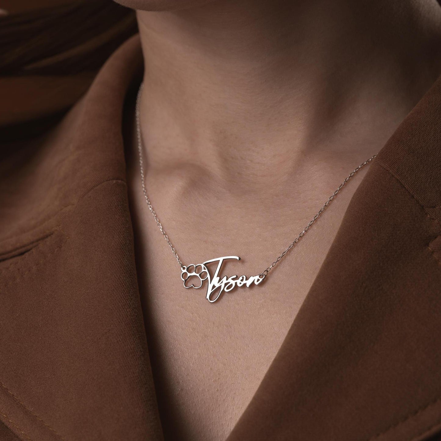 Custom pet name necklace with a paw print design in 925 sterling silver and 14k gold plated options, perfect for pet lovers. A personalized, handmade gift displayed on a soft fabric background.