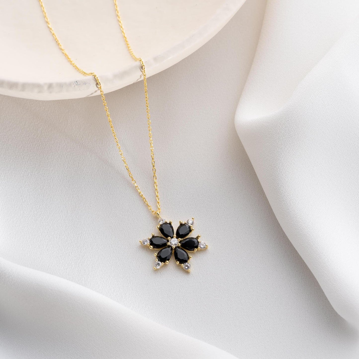 Elegant black flower necklace with genuine zircon stones, available in 925 sterling silver and 14K gold plated options, displayed on a white satin background.
