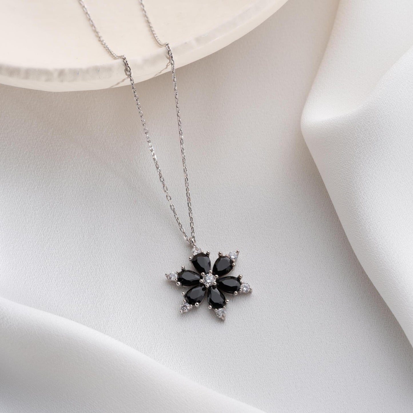 Elegant black flower necklace with genuine zircon stones, available in 925 sterling silver and 14K gold plated options, displayed on a white satin background.