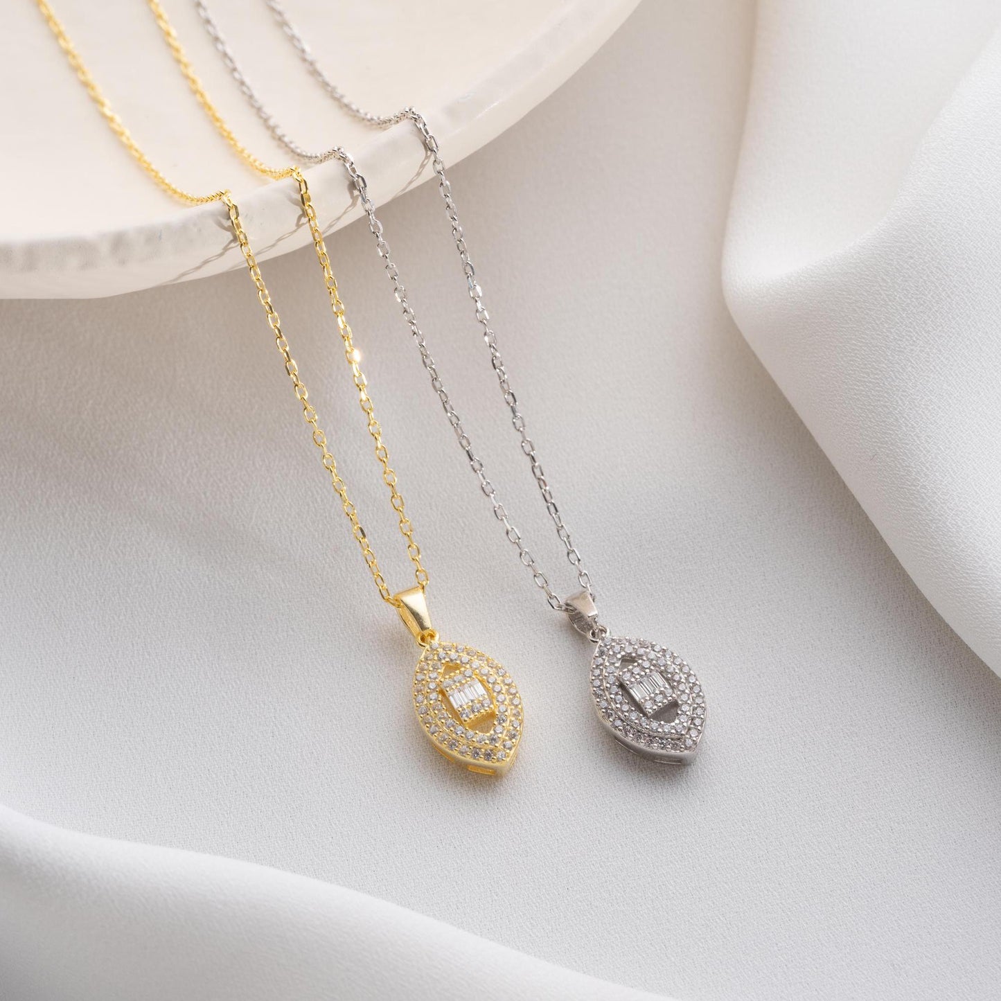 Elegant oval pendant necklace with cubic zirconia stones, available in 925 sterling silver and 14K gold plated options, displayed on a white satin background.