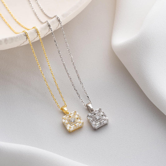 Square pendant necklace with cubic zirconia stones, available in 925 sterling silver and 14K gold plated options, displayed on a white satin background.
