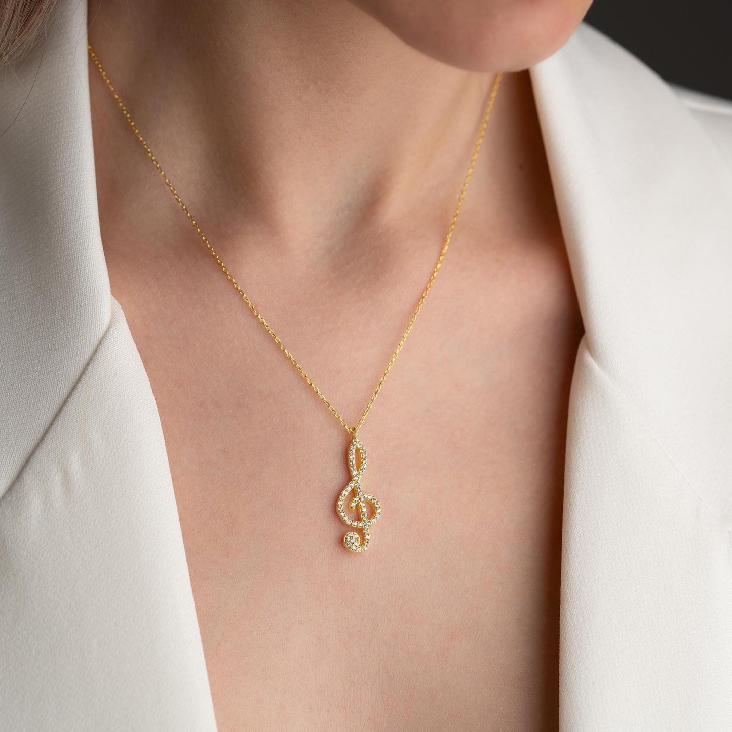 Music note necklace with cubic zirconia stones, available in 925 sterling silver and 14K gold plated options, displayed on a white satin background.