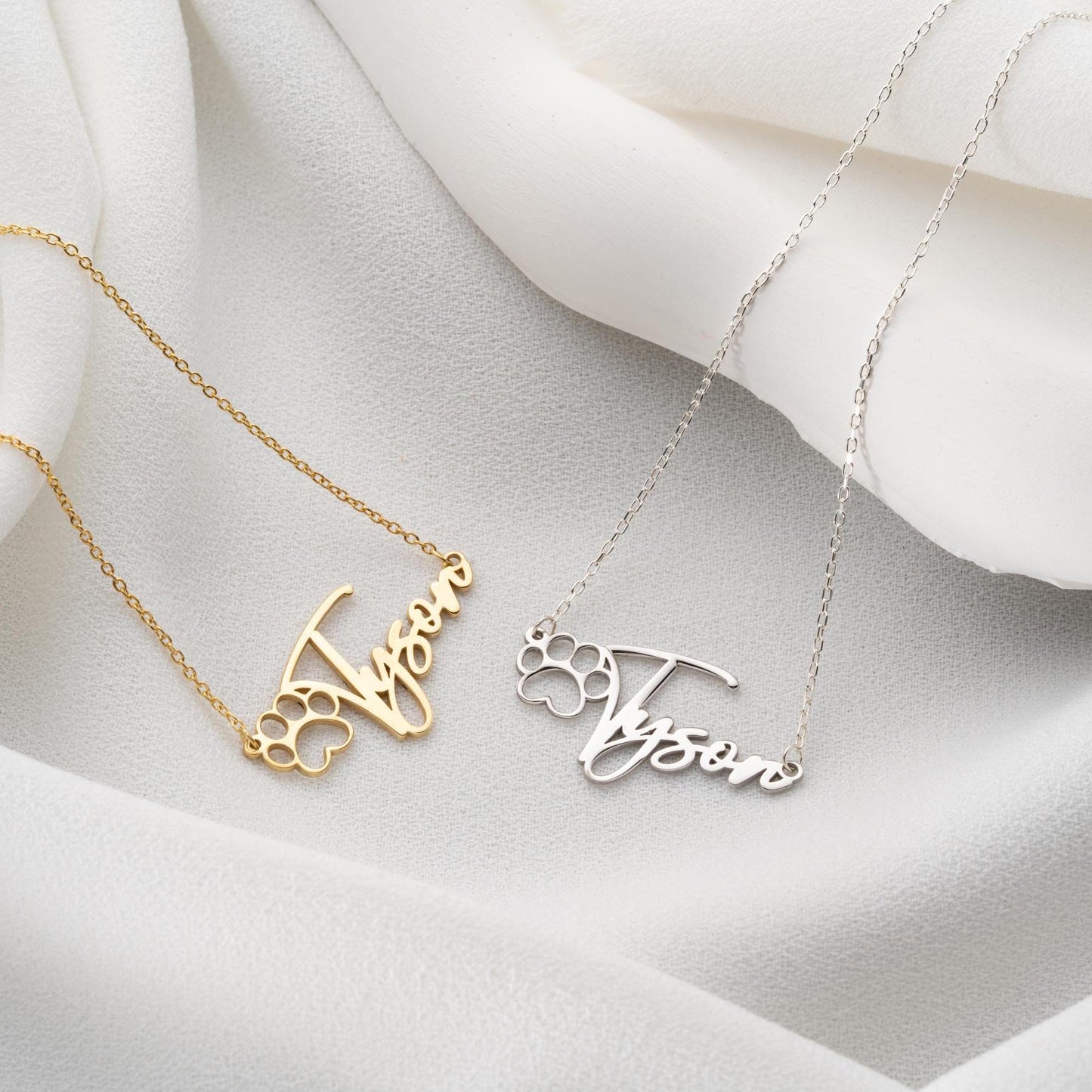 Custom pet name necklace with a paw print design in 925 sterling silver and 14k gold plated options, perfect for pet lovers. A personalized, handmade gift displayed on a soft fabric background.