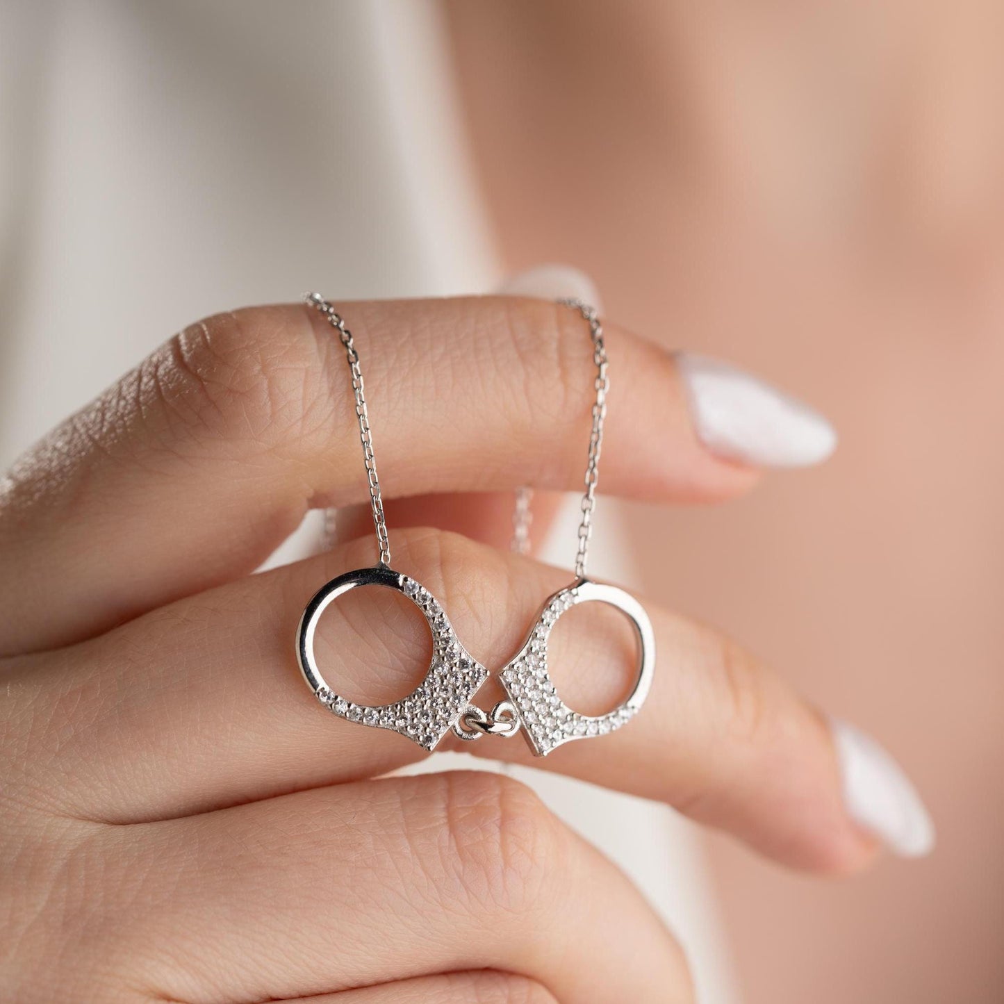 Handcuff necklace with cubic zirconia stones, available in 925 sterling silver and 14K gold plated options, displayed on a white satin background.