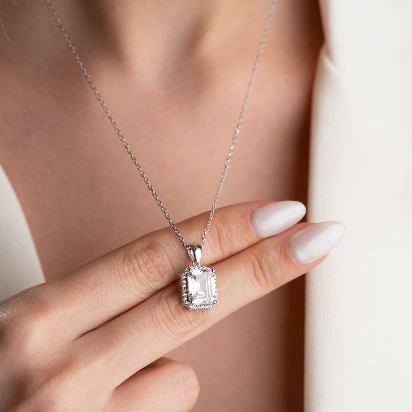Emerald-cut pendant necklace with cubic zirconia stones, available in 925 sterling silver and 14K gold plated options, displayed on a white satin background.