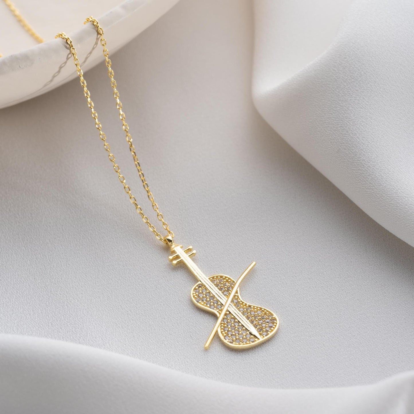 Violin-shaped necklace with cubic zirconia stones, available in 925 sterling silver and 14K gold plated options, displayed on a white satin background.