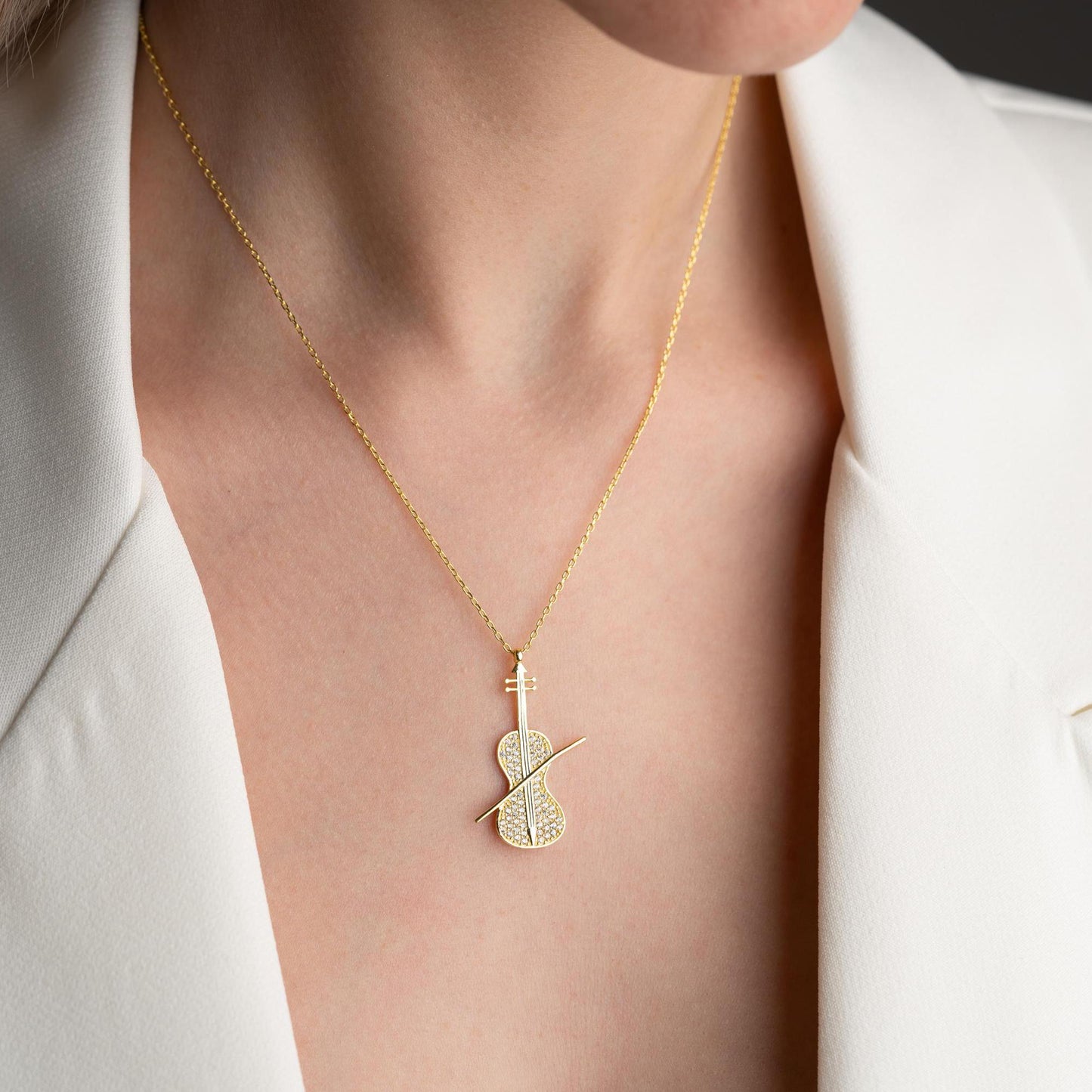 Violin-shaped necklace with cubic zirconia stones, available in 925 sterling silver and 14K gold plated options, displayed on a white satin background.