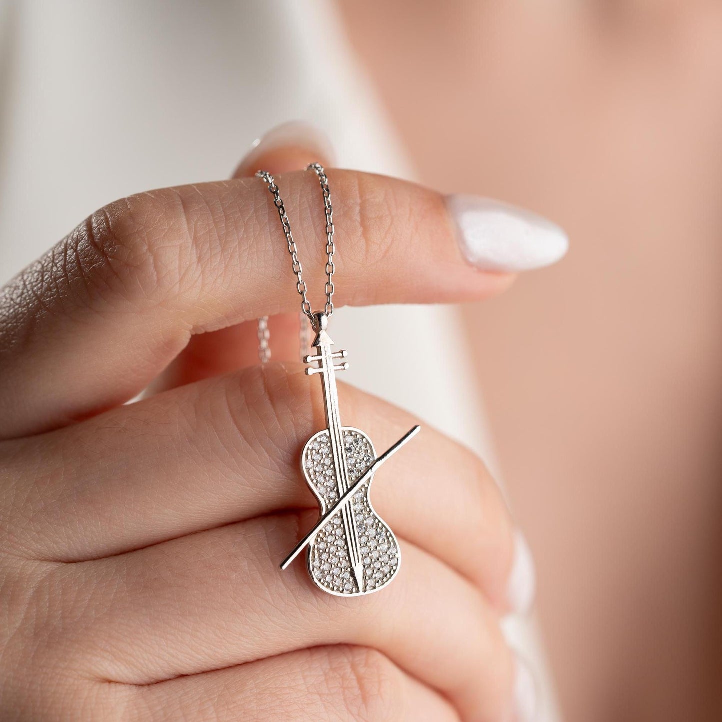 Violin-shaped necklace with cubic zirconia stones, available in 925 sterling silver and 14K gold plated options, displayed on a white satin background.