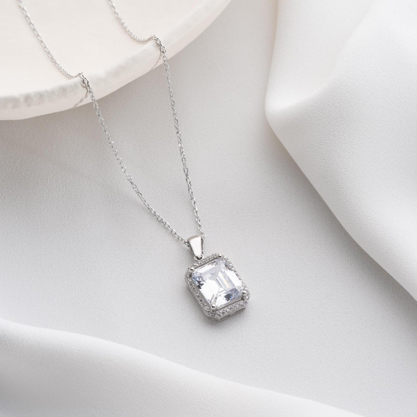 Emerald-cut pendant necklace with cubic zirconia stones, available in 925 sterling silver and 14K gold plated options, displayed on a white satin background