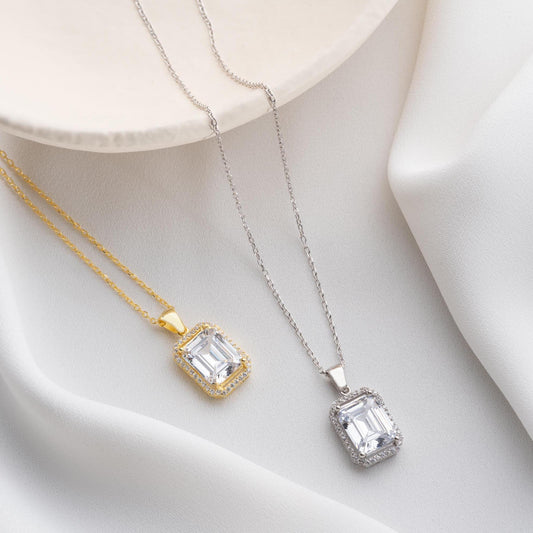 Emerald-cut pendant necklace with cubic zirconia stones, available in 925 sterling silver and 14K gold plated options, displayed on a white satin background