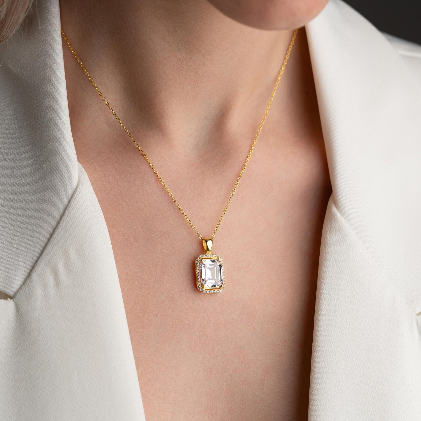 Emerald-cut pendant necklace with cubic zirconia stones, available in 925 sterling silver and 14K gold plated options, displayed on a white satin background