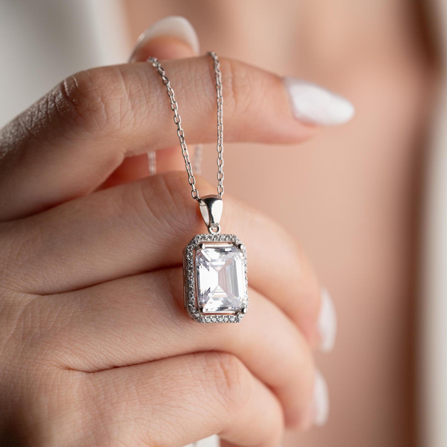 Emerald-cut pendant necklace with cubic zirconia stones, available in 925 sterling silver and 14K gold plated options, displayed on a white satin background