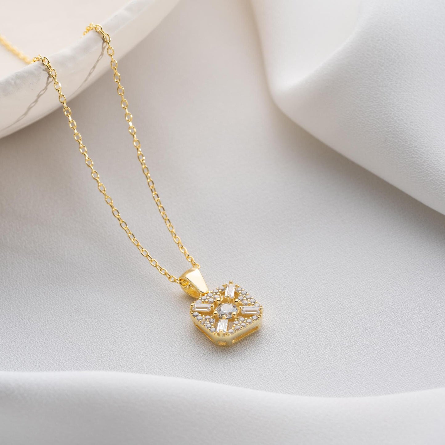 Square pendant necklace with cubic zirconia stones, available in 925 sterling silver and 14K gold plated options, displayed on a white satin background