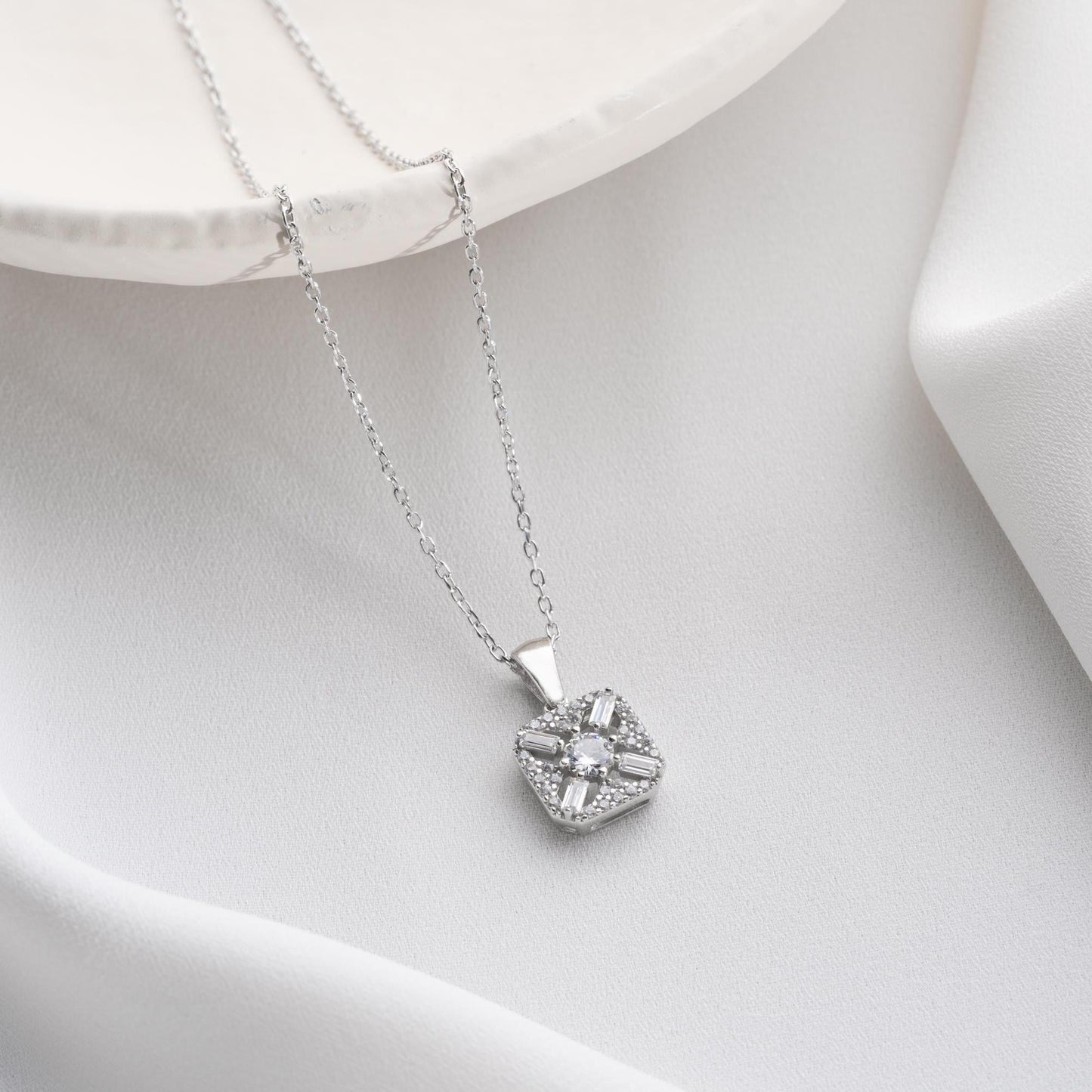 Square pendant necklace with cubic zirconia stones, available in 925 sterling silver and 14K gold plated options, displayed on a white satin background