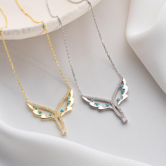 Angel wing necklace with turquoise and cubic zirconia stones, available in 925 sterling silver and 14K gold plated options, displayed on a white satin background