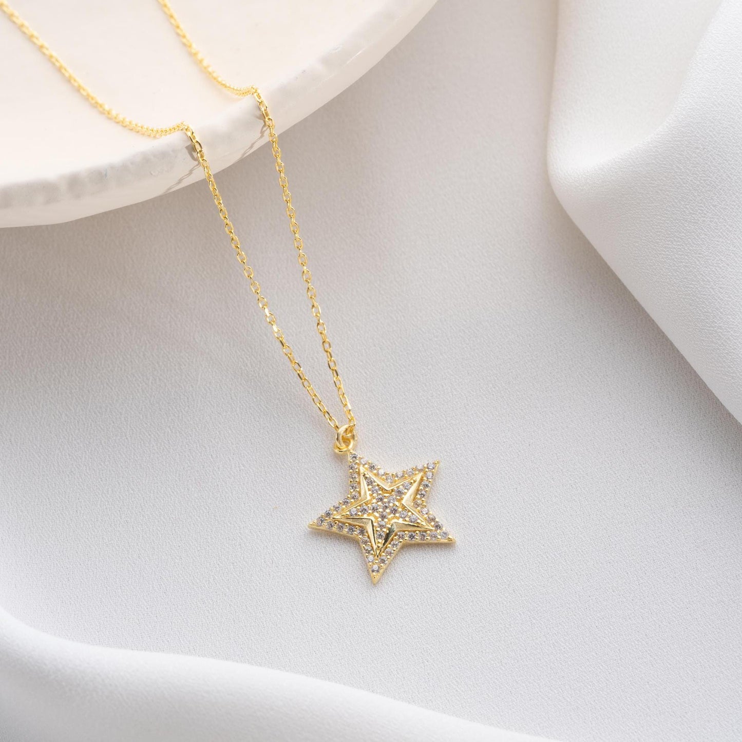 Star pendant necklace with cubic zirconia stones, available in 925 sterling silver and 14K gold plated options, displayed on a white satin background.