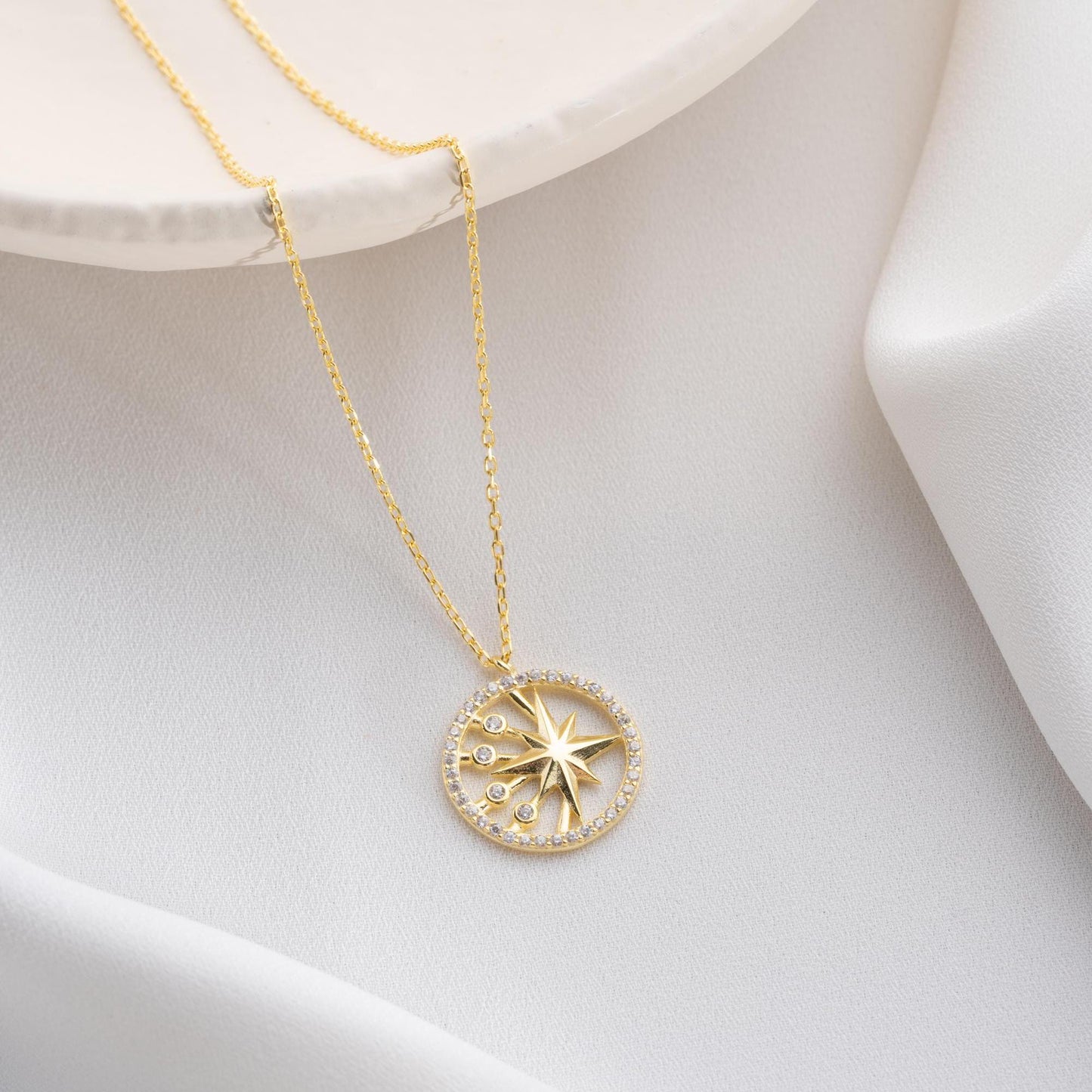 North Star pendant necklace with cubic zirconia stones, available in 925 sterling silver and 14K gold plated options, displayed on a white satin background