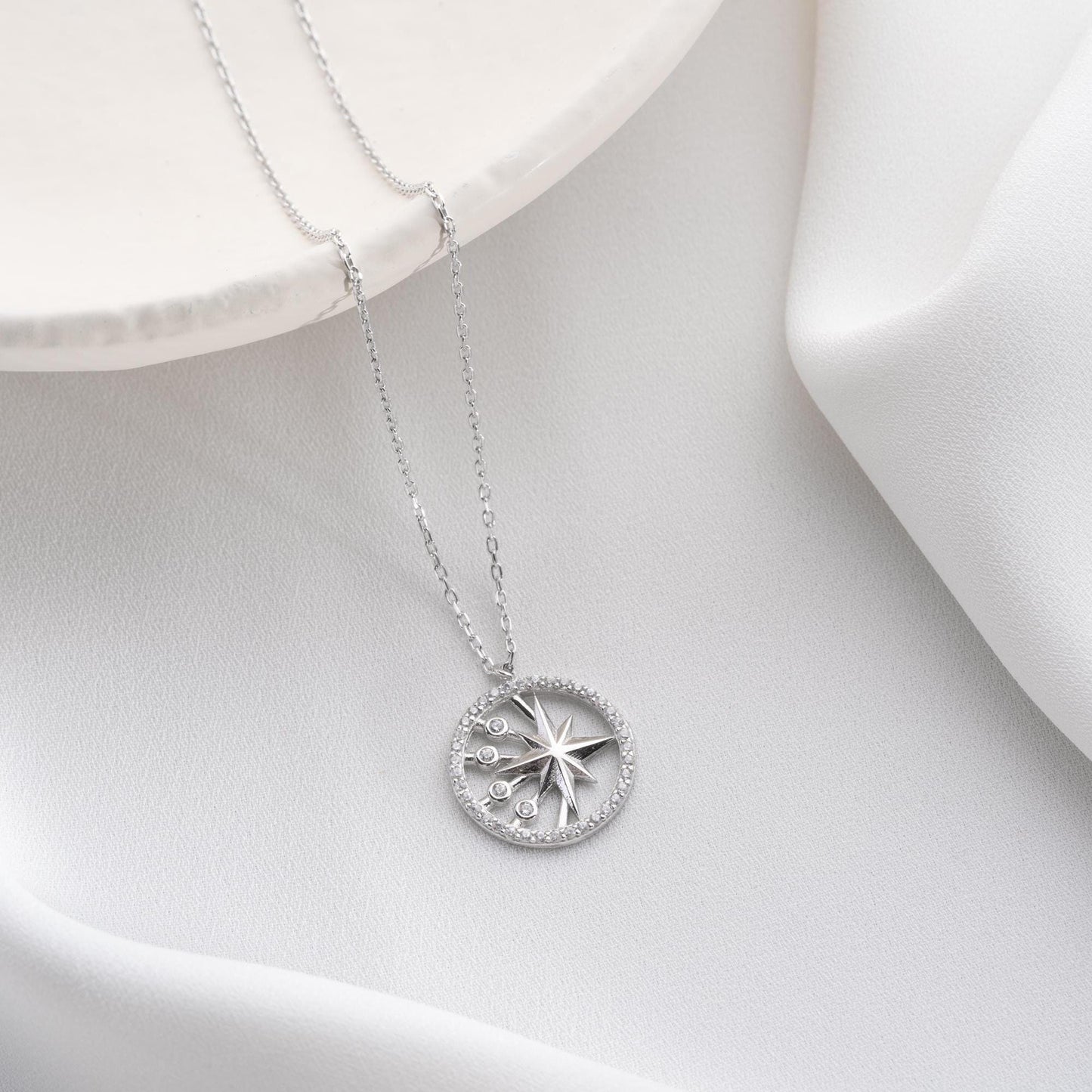 North Star pendant necklace with cubic zirconia stones, available in 925 sterling silver and 14K gold plated options, displayed on a white satin background