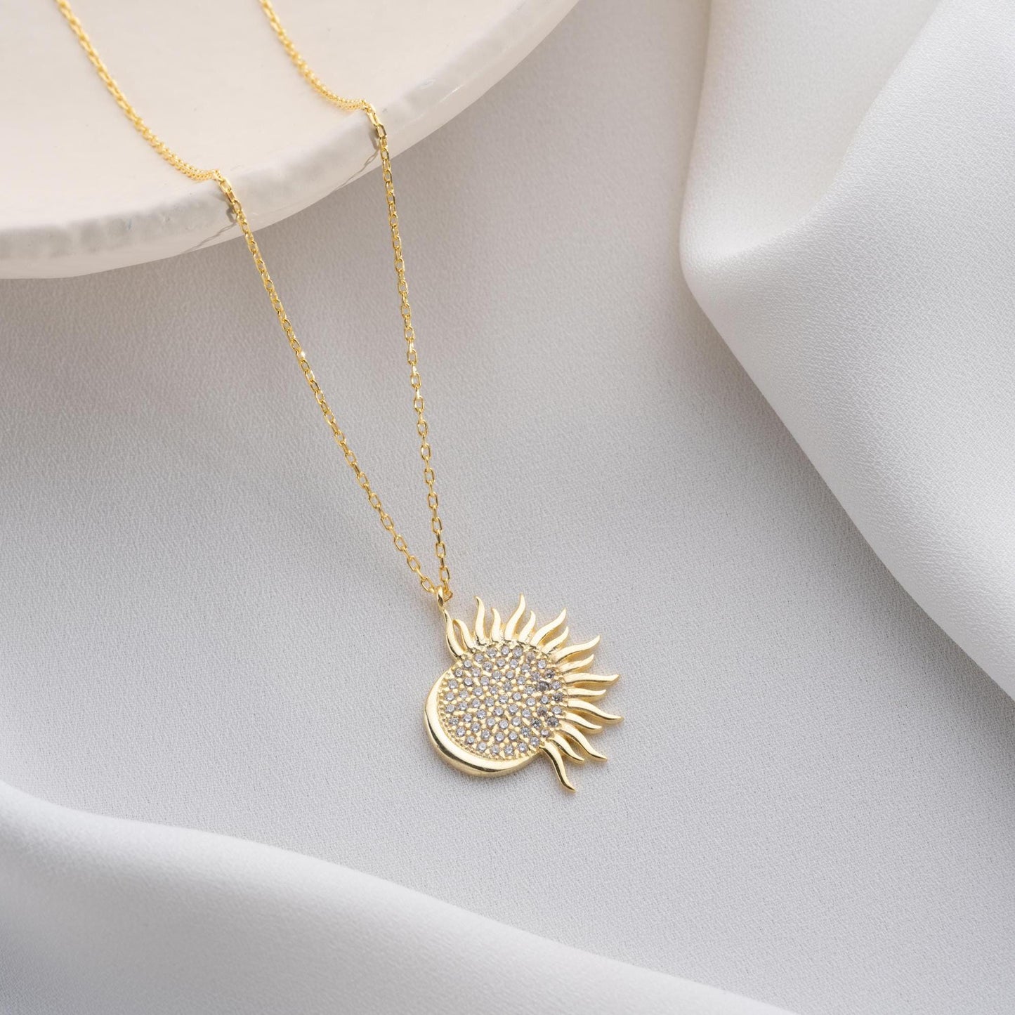 Sun pendant necklace with cubic zirconia stones, available in 925 sterling silver and 14K gold plated options, displayed on a white satin background
