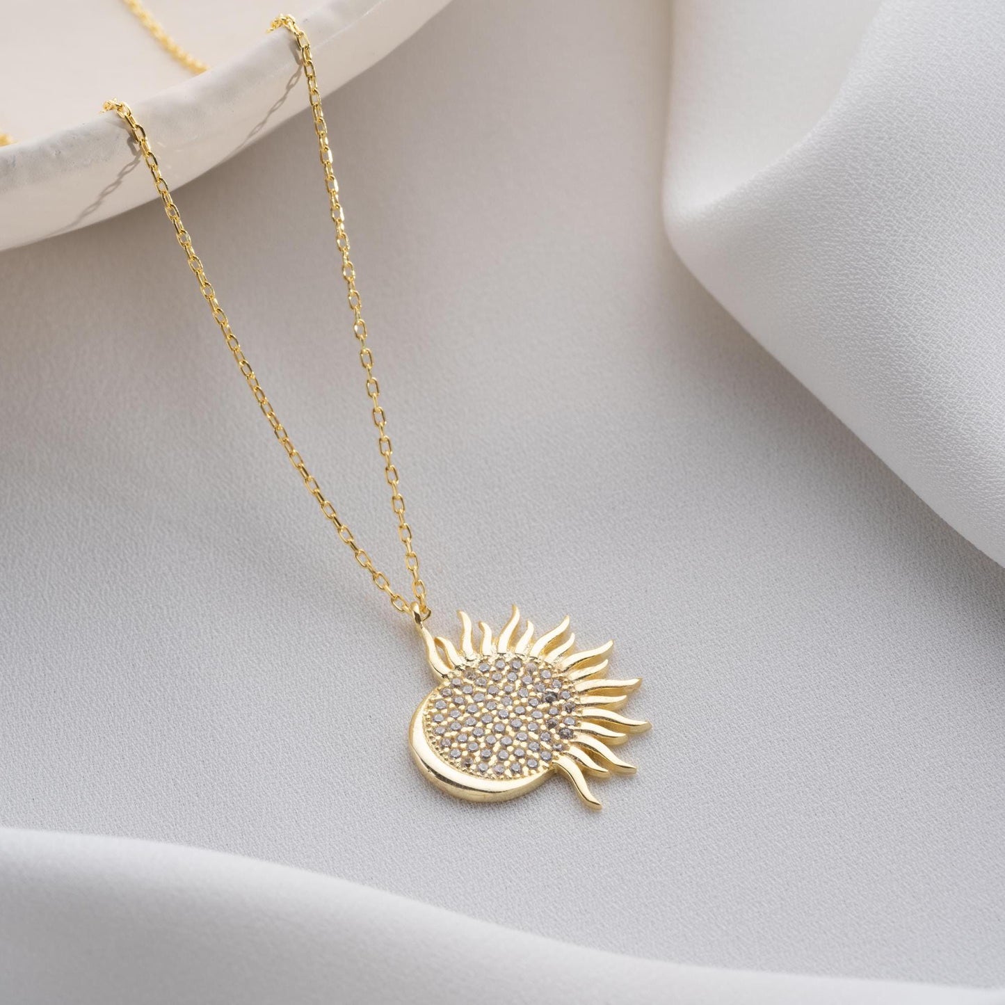 Sun pendant necklace with cubic zirconia stones, available in 925 sterling silver and 14K gold plated options, displayed on a white satin background