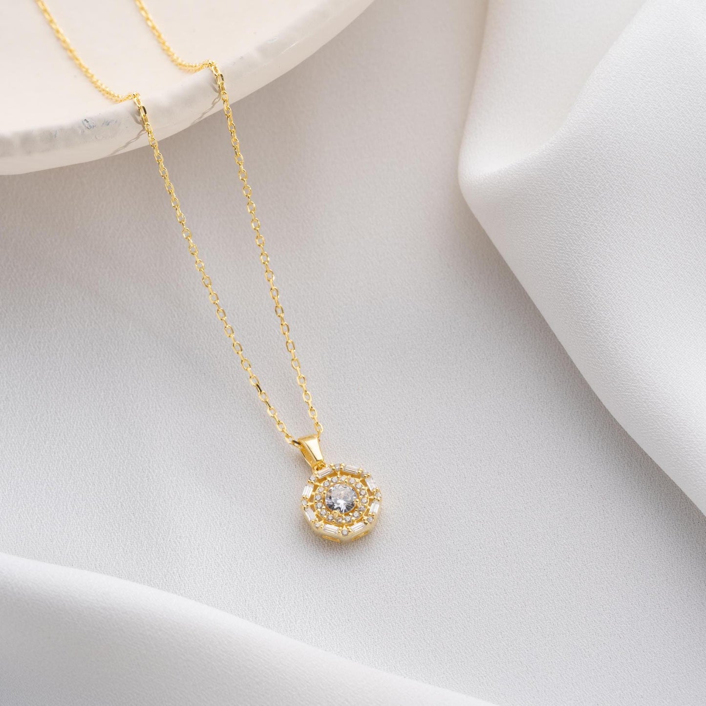 Halo pendant necklace with cubic zirconia stones, available in 925 sterling silver and 14K gold plated options, displayed on a white satin background.