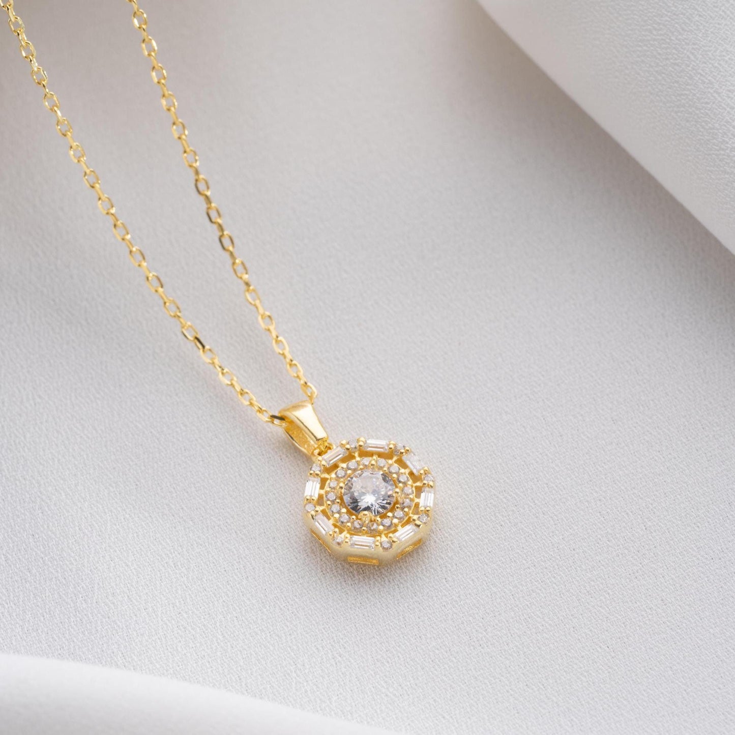Halo pendant necklace with cubic zirconia stones, available in 925 sterling silver and 14K gold plated options, displayed on a white satin background.