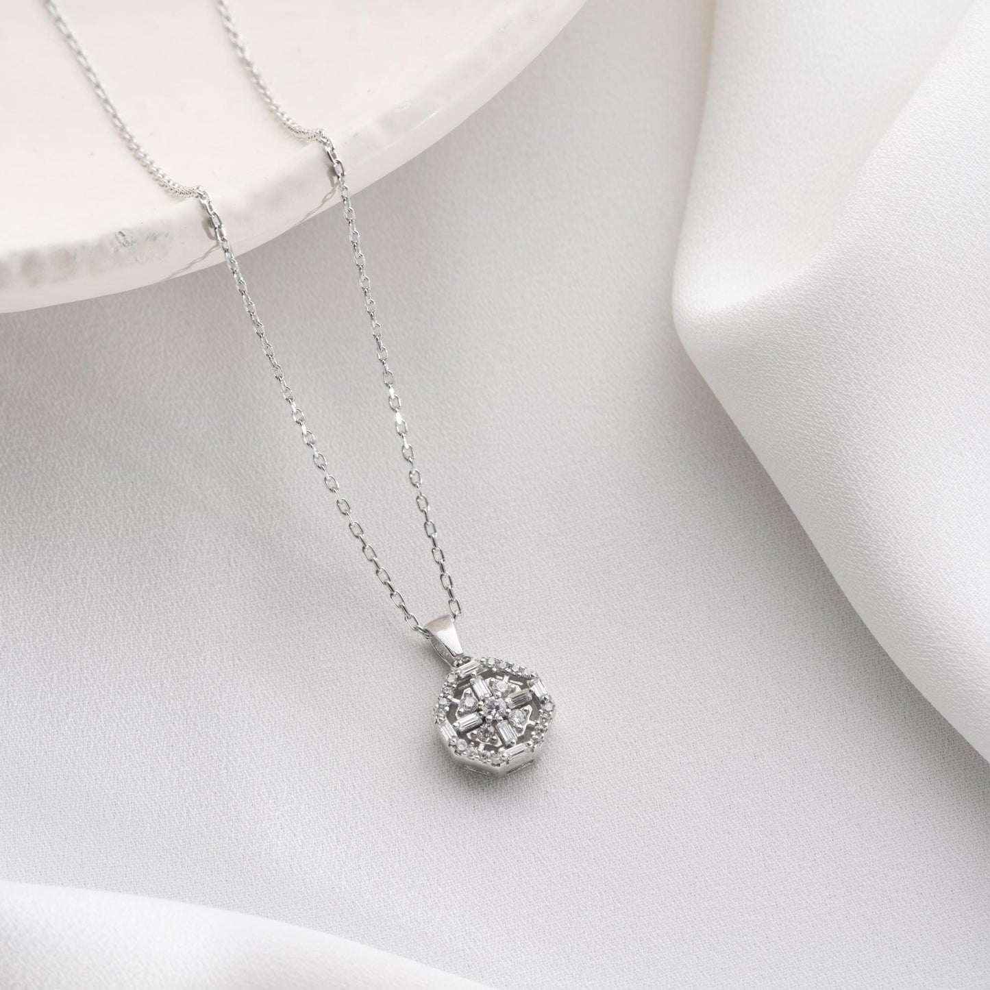 Octagon pendant necklace with cubic zirconia stones, available in 925 sterling silver and 14K gold plated options, displayed on a white satin background