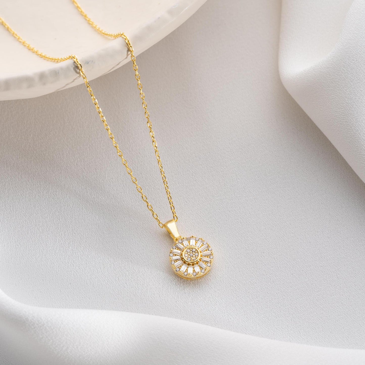 Sunburst pendant necklace with cubic zirconia, available in 925 sterling silver and 14K gold plated options, displayed on a soft satin background