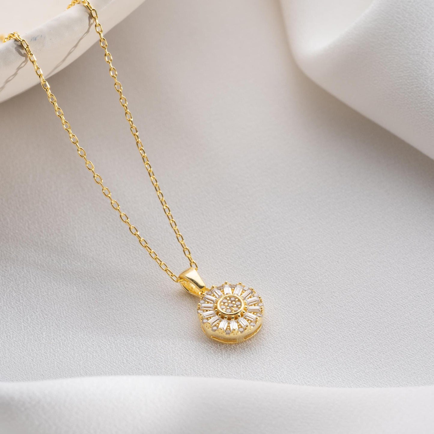 Sunburst pendant necklace with cubic zirconia, available in 925 sterling silver and 14K gold plated options, displayed on a soft satin background