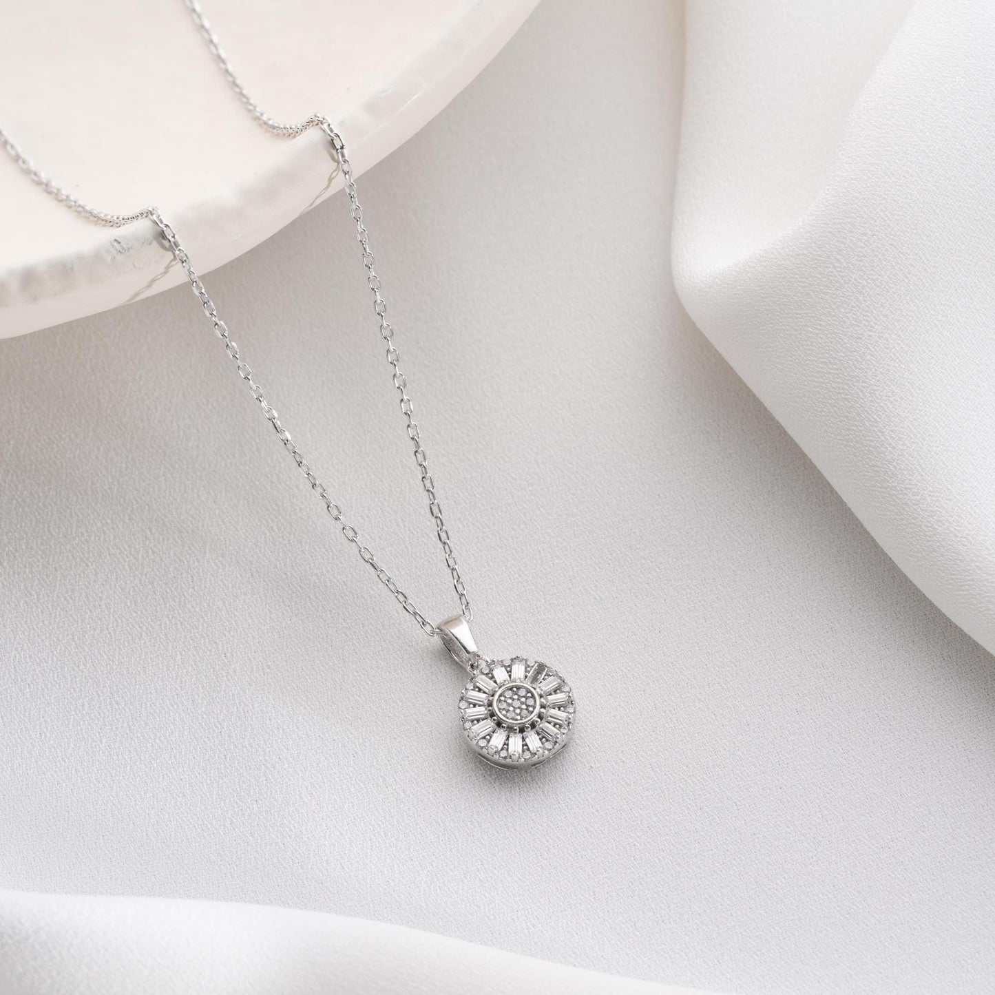 Sunburst pendant necklace with cubic zirconia, available in 925 sterling silver and 14K gold plated options, displayed on a soft satin background