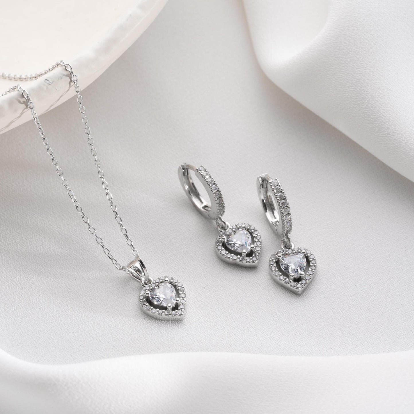 Heart pendant necklace and earrings set, crafted in 925 sterling silver with cubic zirconia stones, displayed on a soft satin background