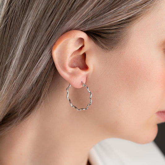 Wavy hoop earrings in 925 sterling silver and 14K gold plated options, displayed on a marble background