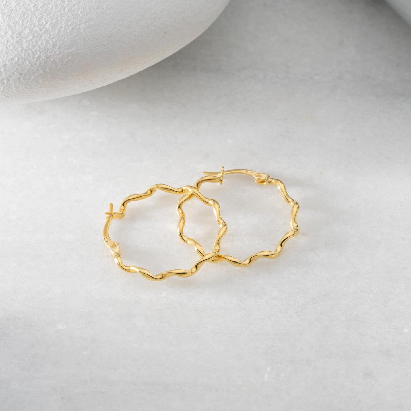 Wavy hoop earrings in 925 sterling silver and 14K gold plated options, displayed on a marble background