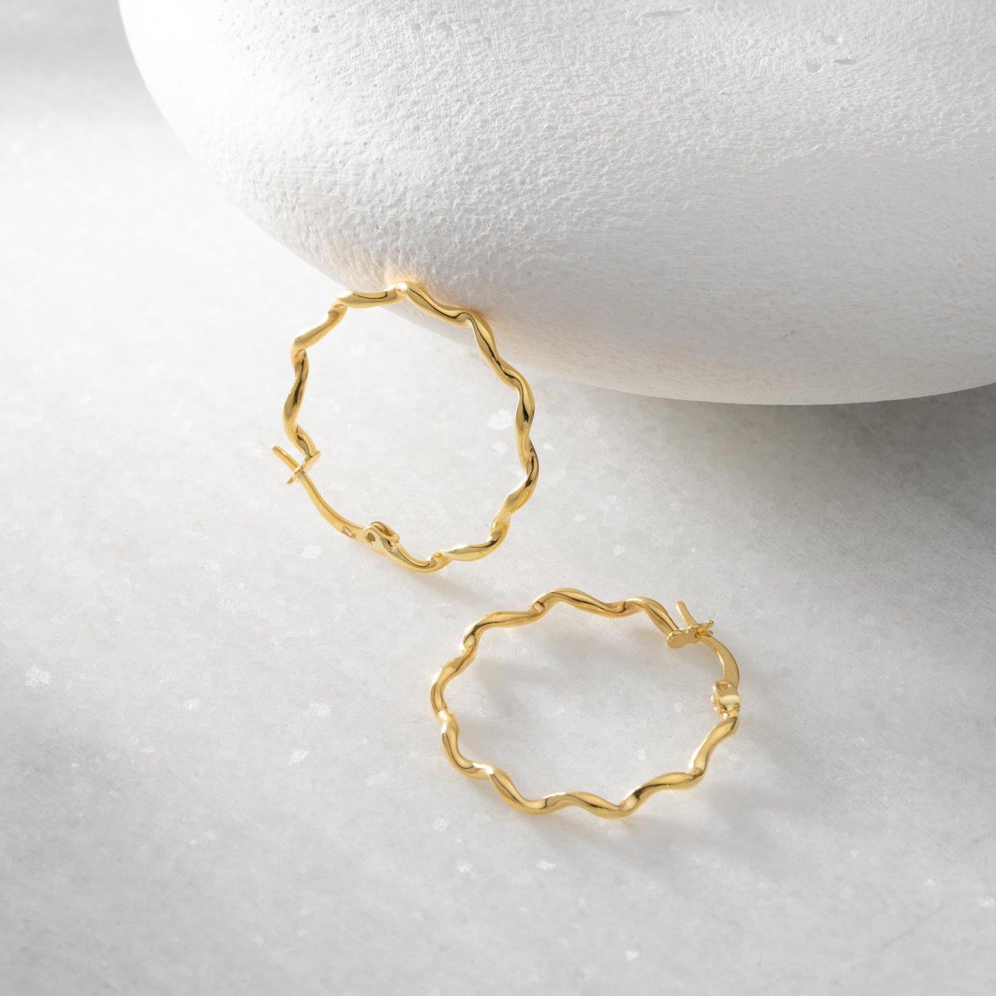 Wavy hoop earrings in 925 sterling silver and 14K gold plated options, displayed on a marble background