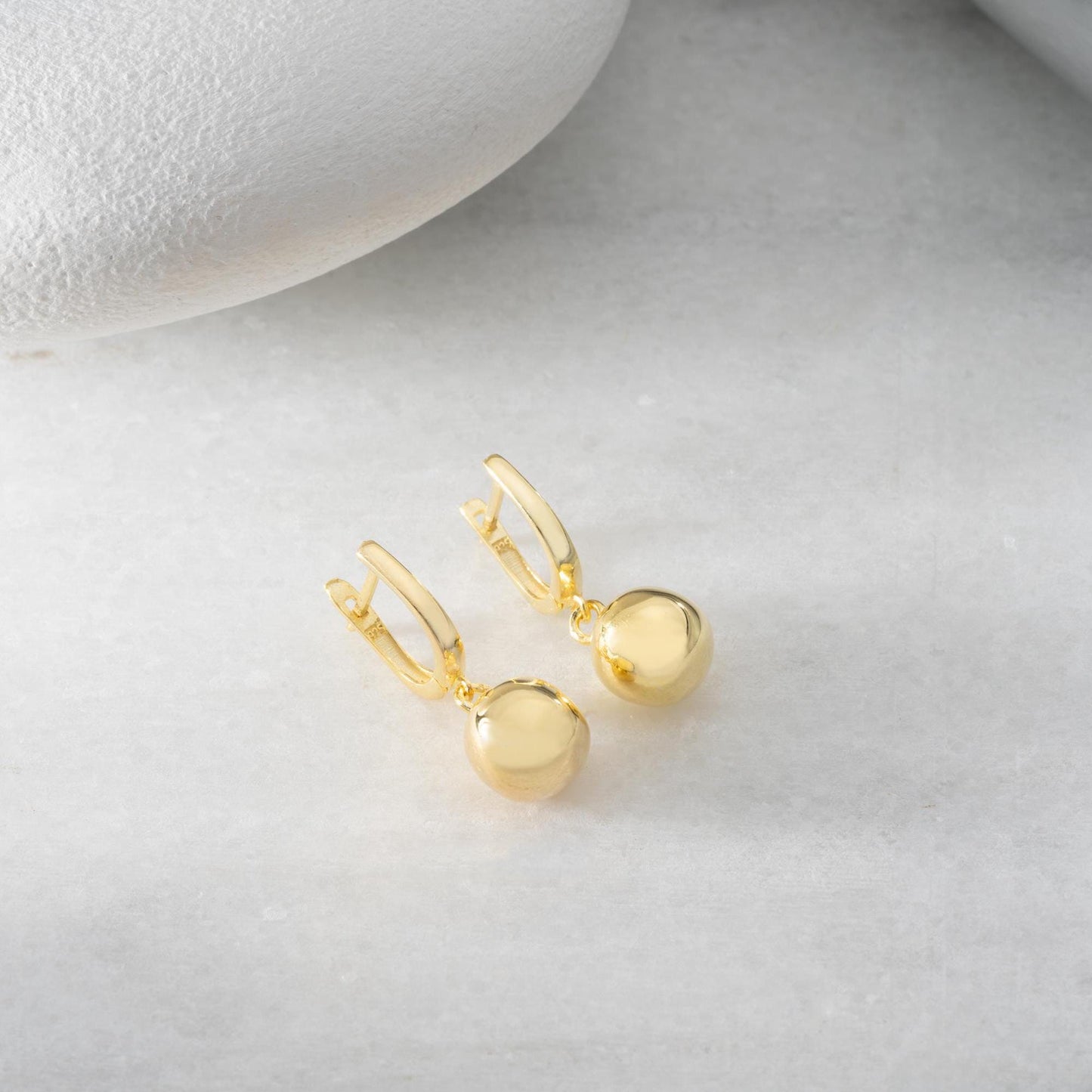 minimalist ball earrings in 925 sterling silver and 14K gold plated options, featuring a sleek design and lever-back closure displayed on a white marble background