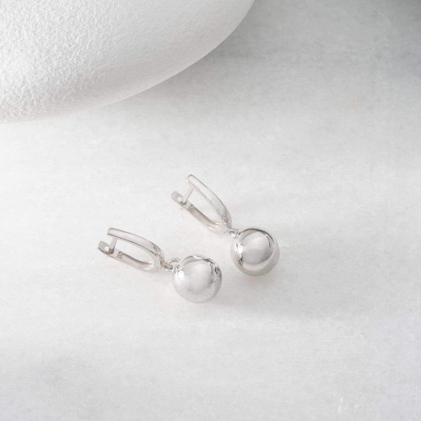 minimalist ball earrings in 925 sterling silver and 14K gold plated options, featuring a sleek design and lever-back closure displayed on a white marble background