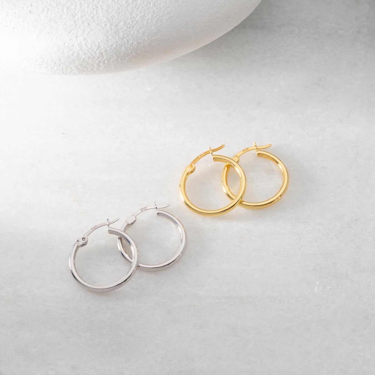 classic hoop earrings in 925 sterling silver and 14K gold plated options, featuring a minimalist polished design displayed on a marble background