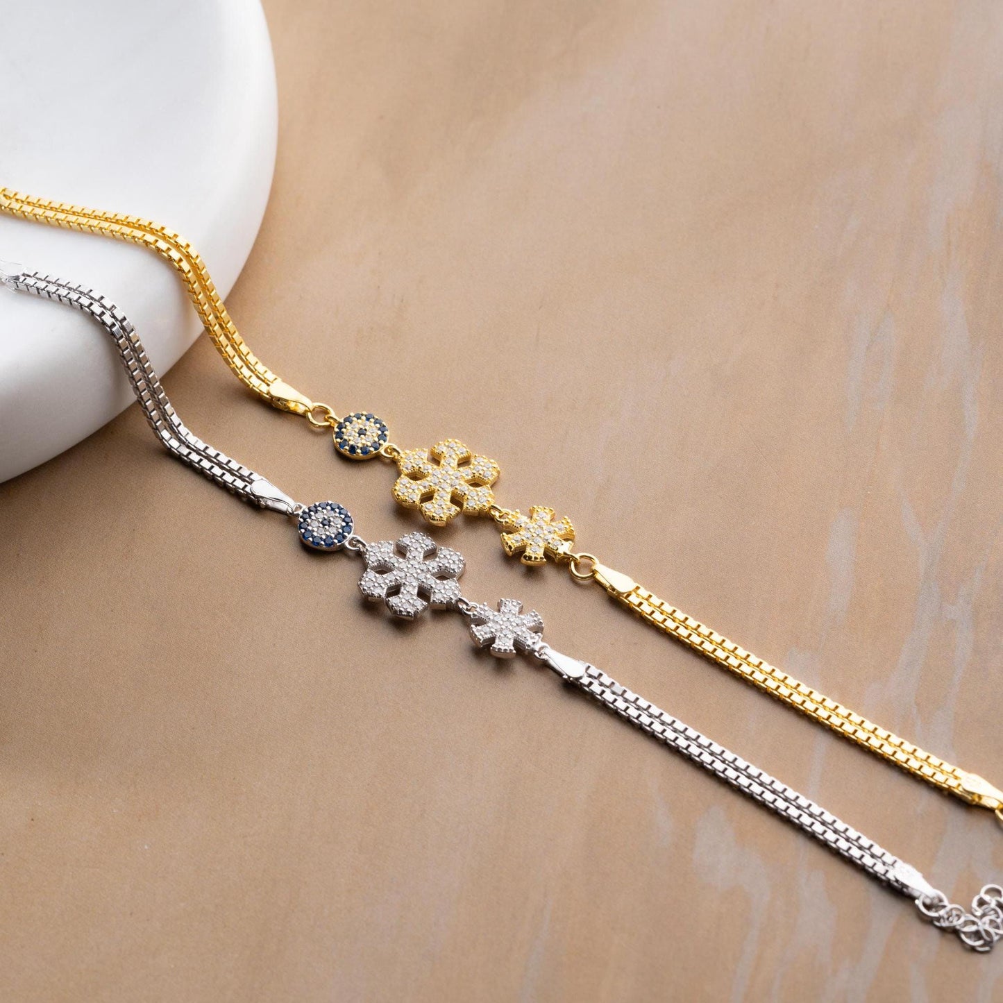 A stunning charm bracelet featuring delicate snowflake motifs and evil eye accents, crafted from 925 Sterling Silver and cubic zirconia stones, available in silver and gold finishes, ideal for festive gifting.