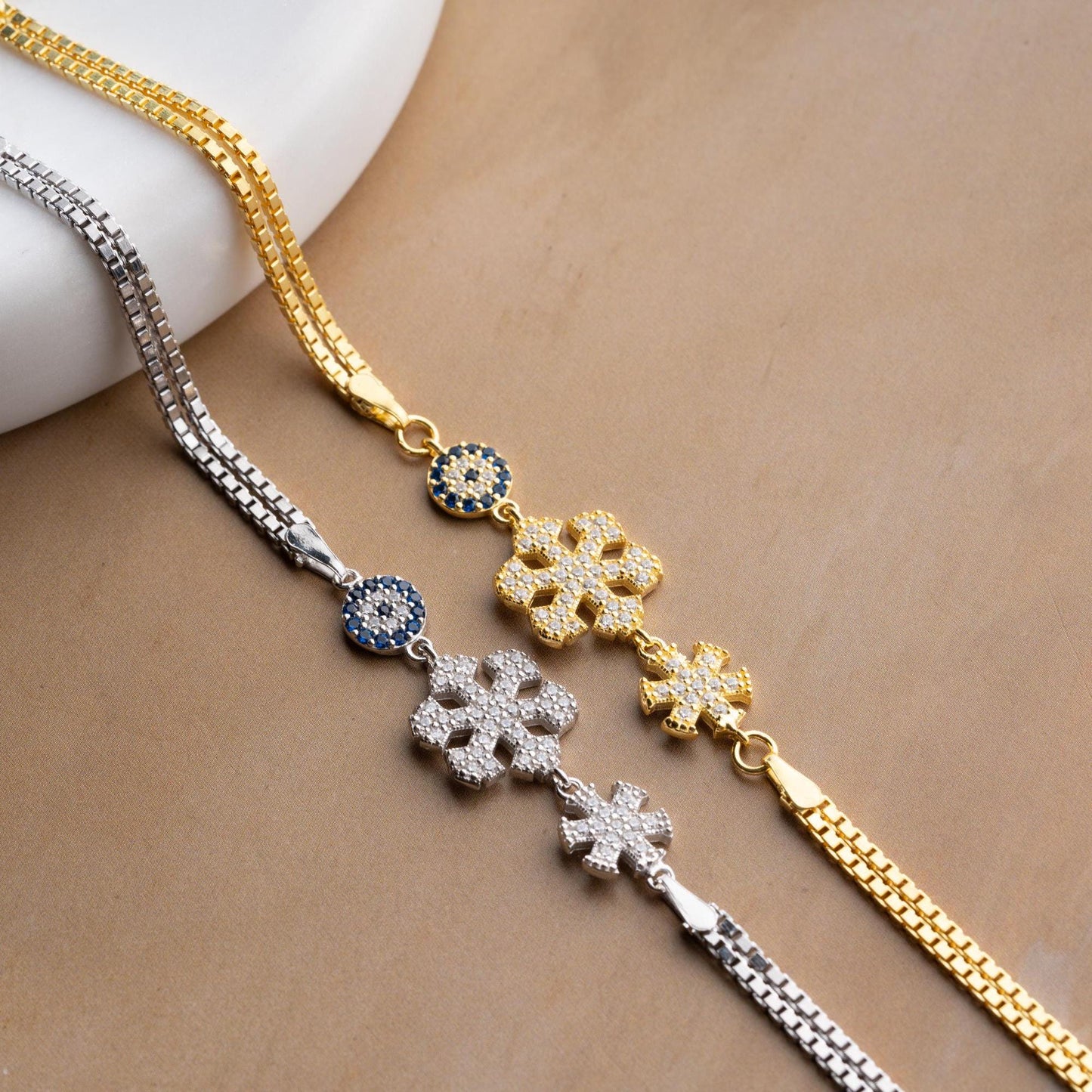 A stunning charm bracelet featuring delicate snowflake motifs and evil eye accents, crafted from 925 Sterling Silver and cubic zirconia stones, available in silver and gold finishes, ideal for festive gifting.