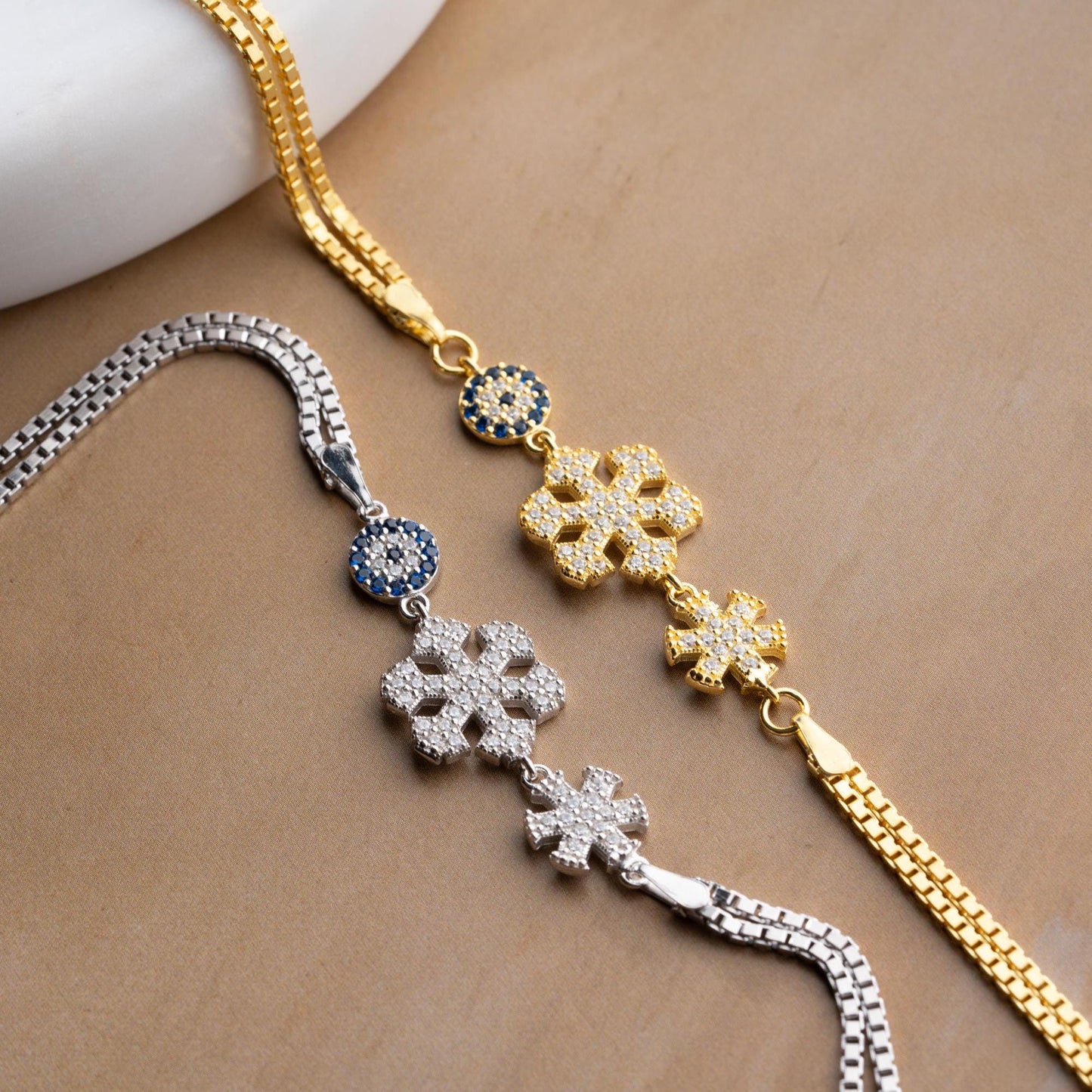 A stunning charm bracelet featuring delicate snowflake motifs and evil eye accents, crafted from 925 Sterling Silver and cubic zirconia stones, available in silver and gold finishes, ideal for festive gifting.