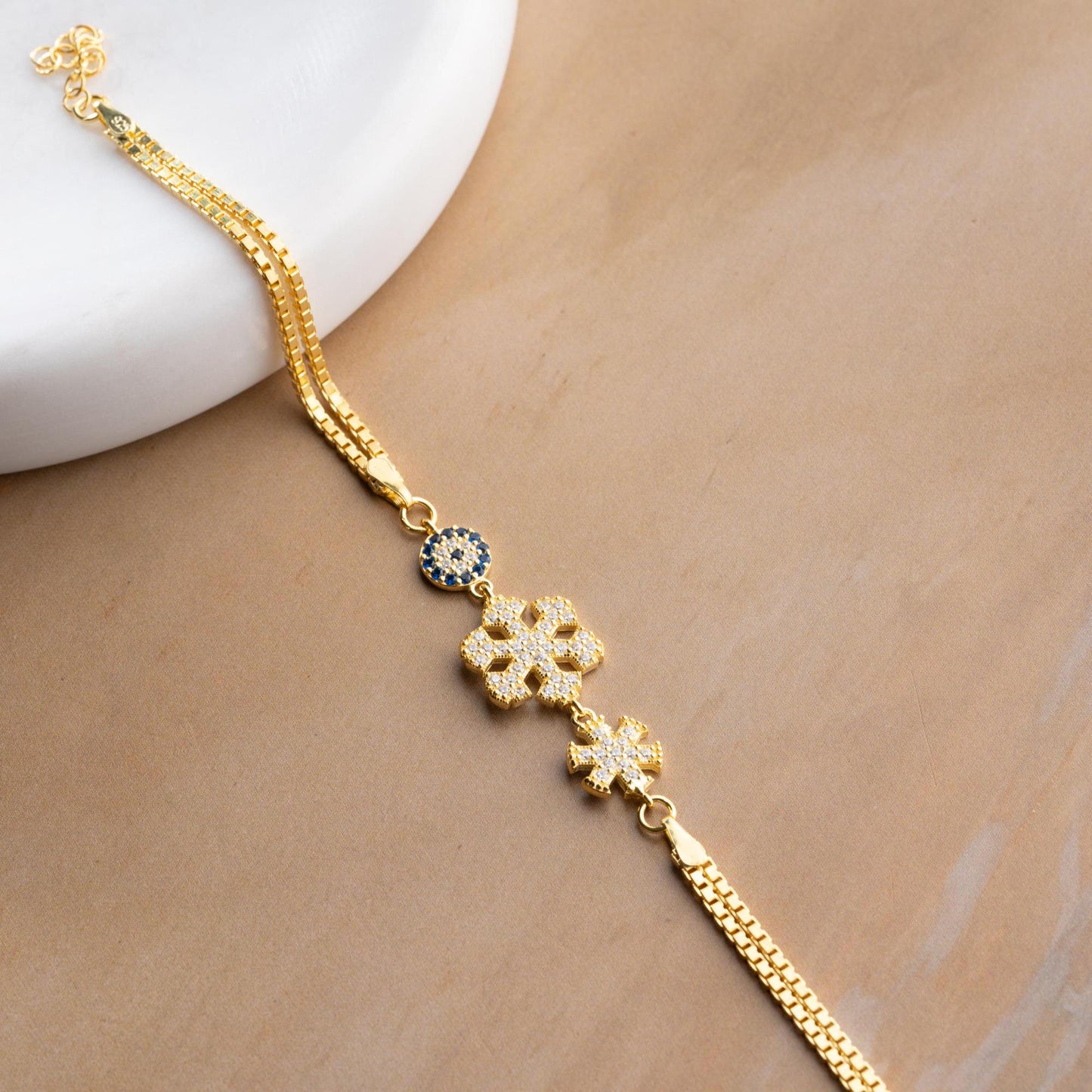 A stunning charm bracelet featuring delicate snowflake motifs and evil eye accents, crafted from 925 Sterling Silver and cubic zirconia stones, available in silver and gold finishes, ideal for festive gifting.