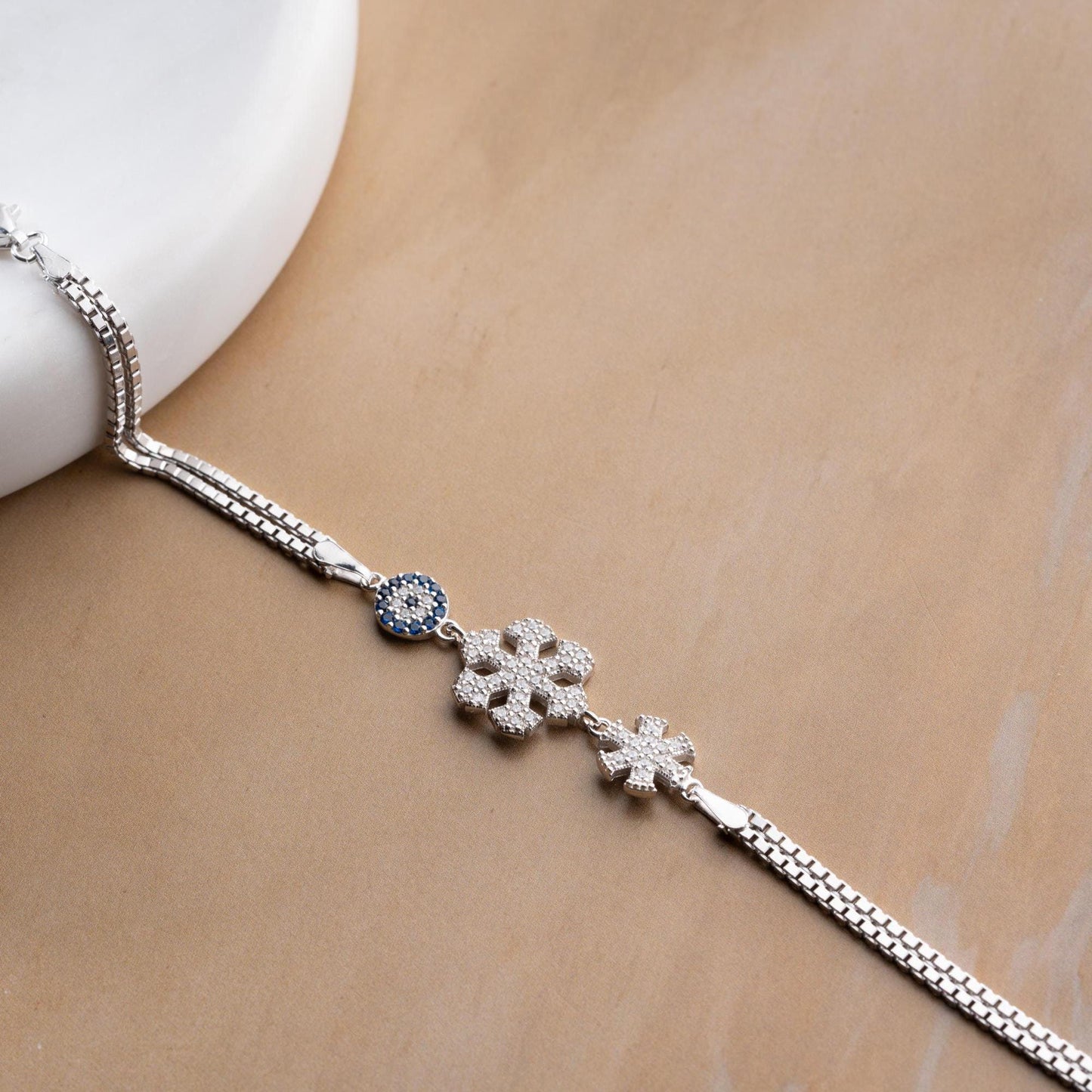 A stunning charm bracelet featuring delicate snowflake motifs and evil eye accents, crafted from 925 Sterling Silver and cubic zirconia stones, available in silver and gold finishes, ideal for festive gifting.