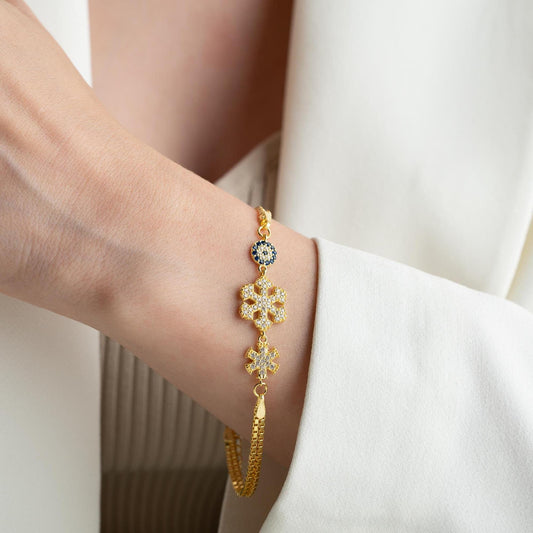 A stunning charm bracelet featuring delicate snowflake motifs and evil eye accents, crafted from 925 Sterling Silver and cubic zirconia stones, available in silver and gold finishes, ideal for festive gifting.