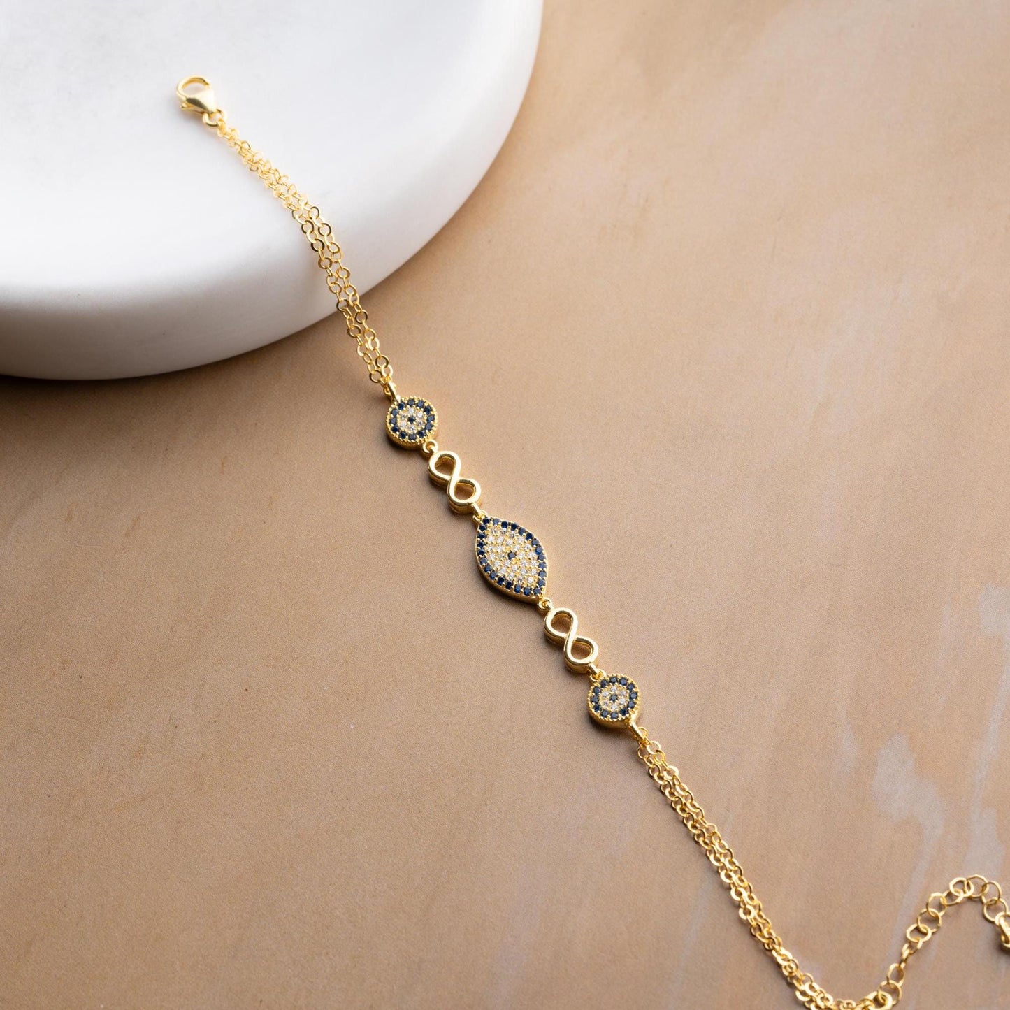 Elegant charm bracelet featuring evil eye and infinity symbols, crafted in 925 Sterling Silver with cubic zirconia stones, available in silver and gold finishes.