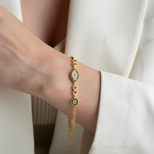 Elegant charm bracelet featuring evil eye and infinity symbols, crafted in 925 Sterling Silver with cubic zirconia stones, available in silver and gold finishes.