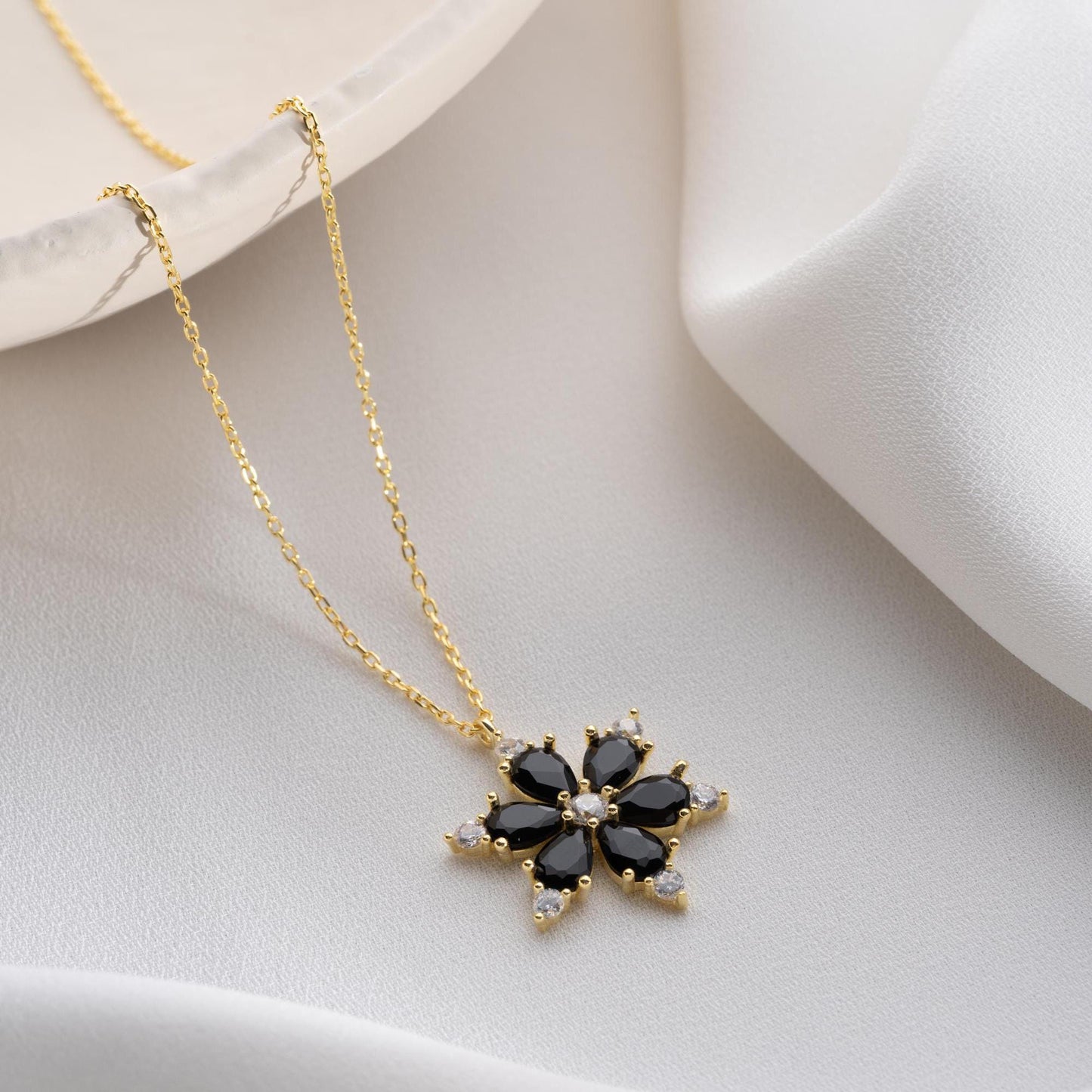 Elegant black flower necklace with genuine zircon stones, available in 925 sterling silver and 14K gold plated options, displayed on a white satin background.