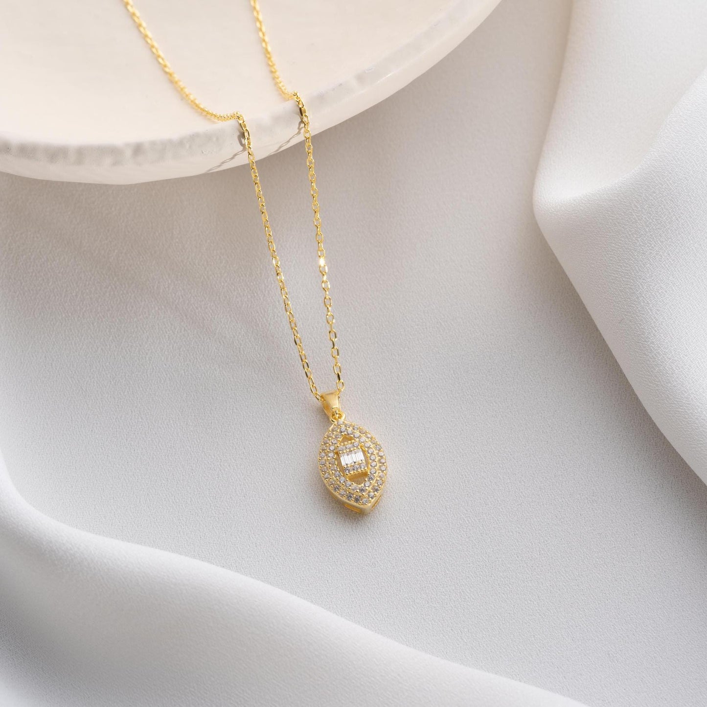 Elegant oval pendant necklace with cubic zirconia stones, available in 925 sterling silver and 14K gold plated options, displayed on a white satin background.