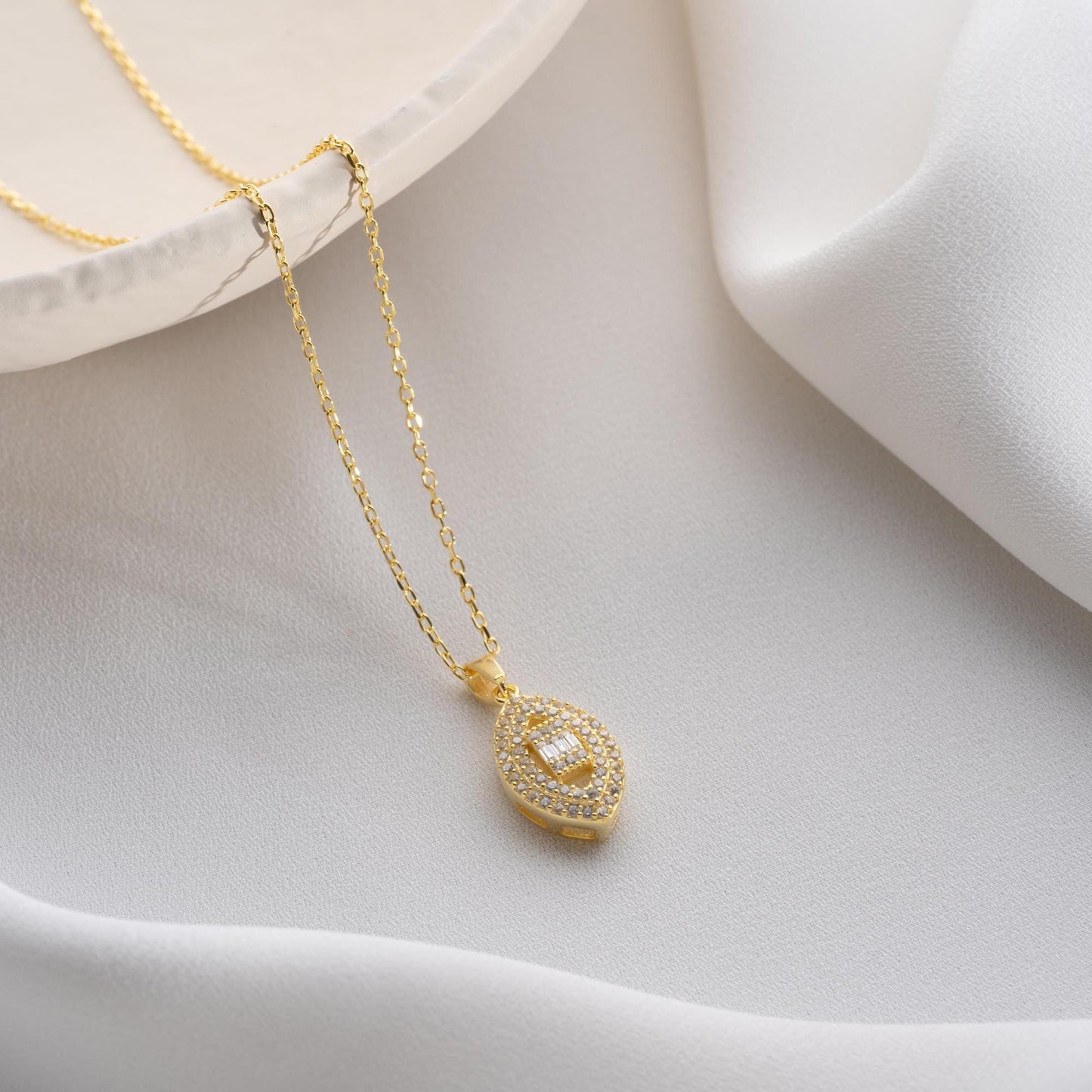 Elegant oval pendant necklace with cubic zirconia stones, available in 925 sterling silver and 14K gold plated options, displayed on a white satin background.